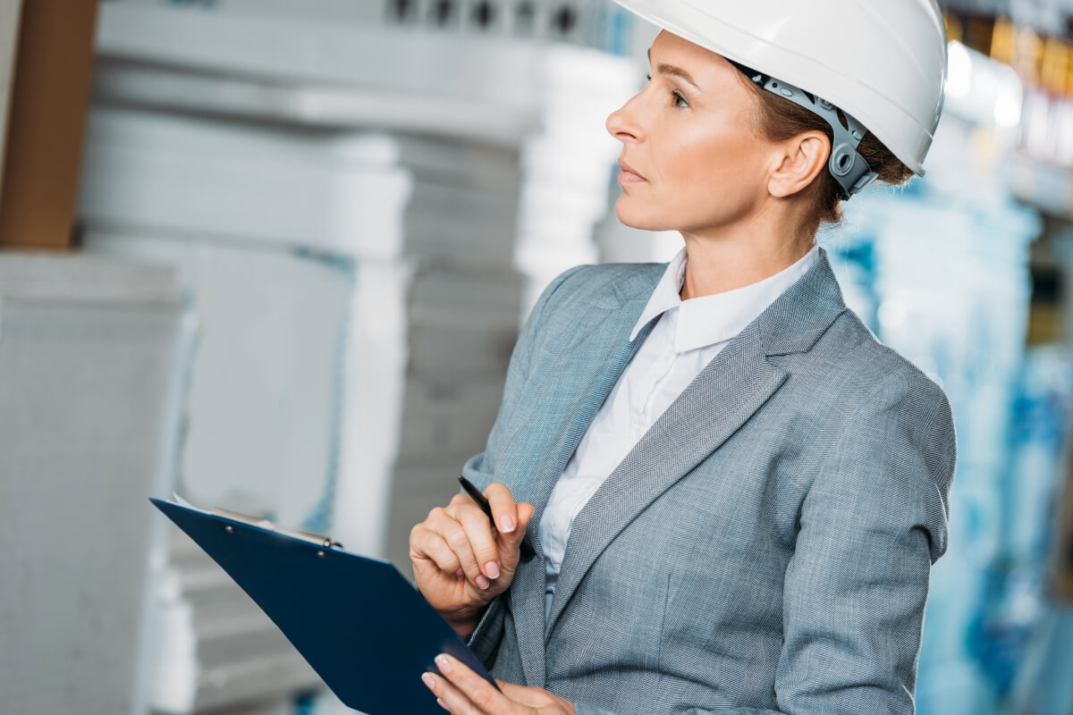 Photo of a person in formal work clothing and a hard hat using a clipboard, representing inspections